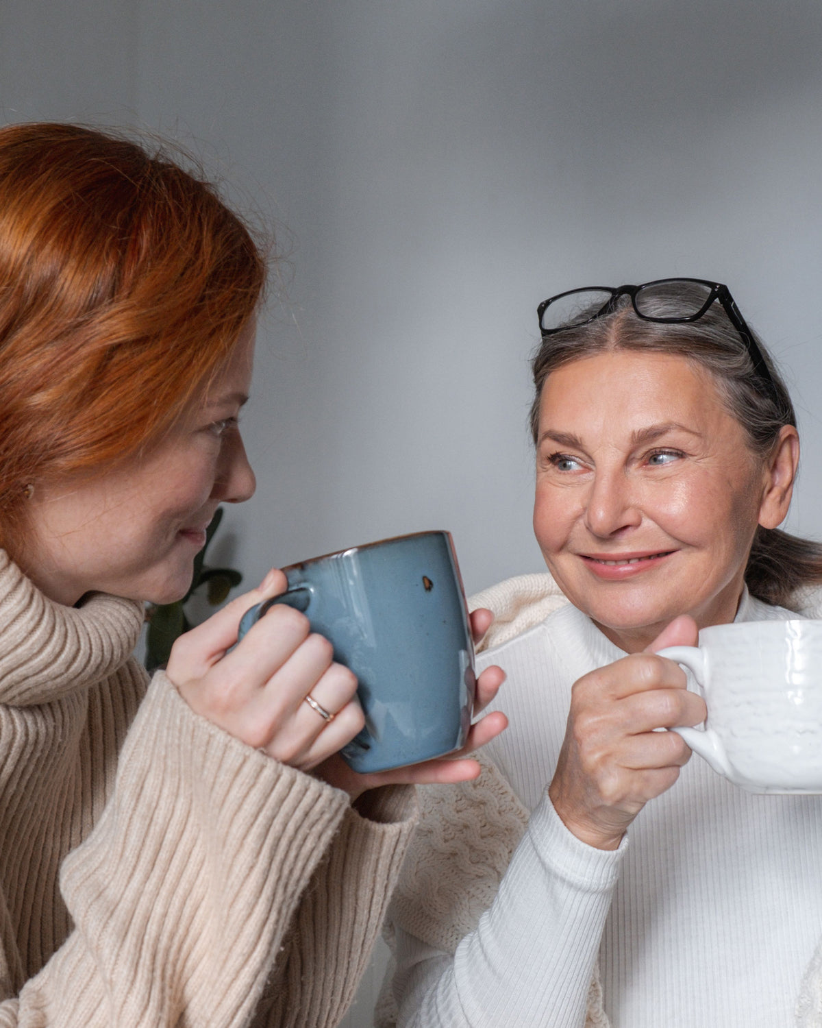 Zwei Frauen lachen gemeinsam, jede mit einer Tasse in der Hand.