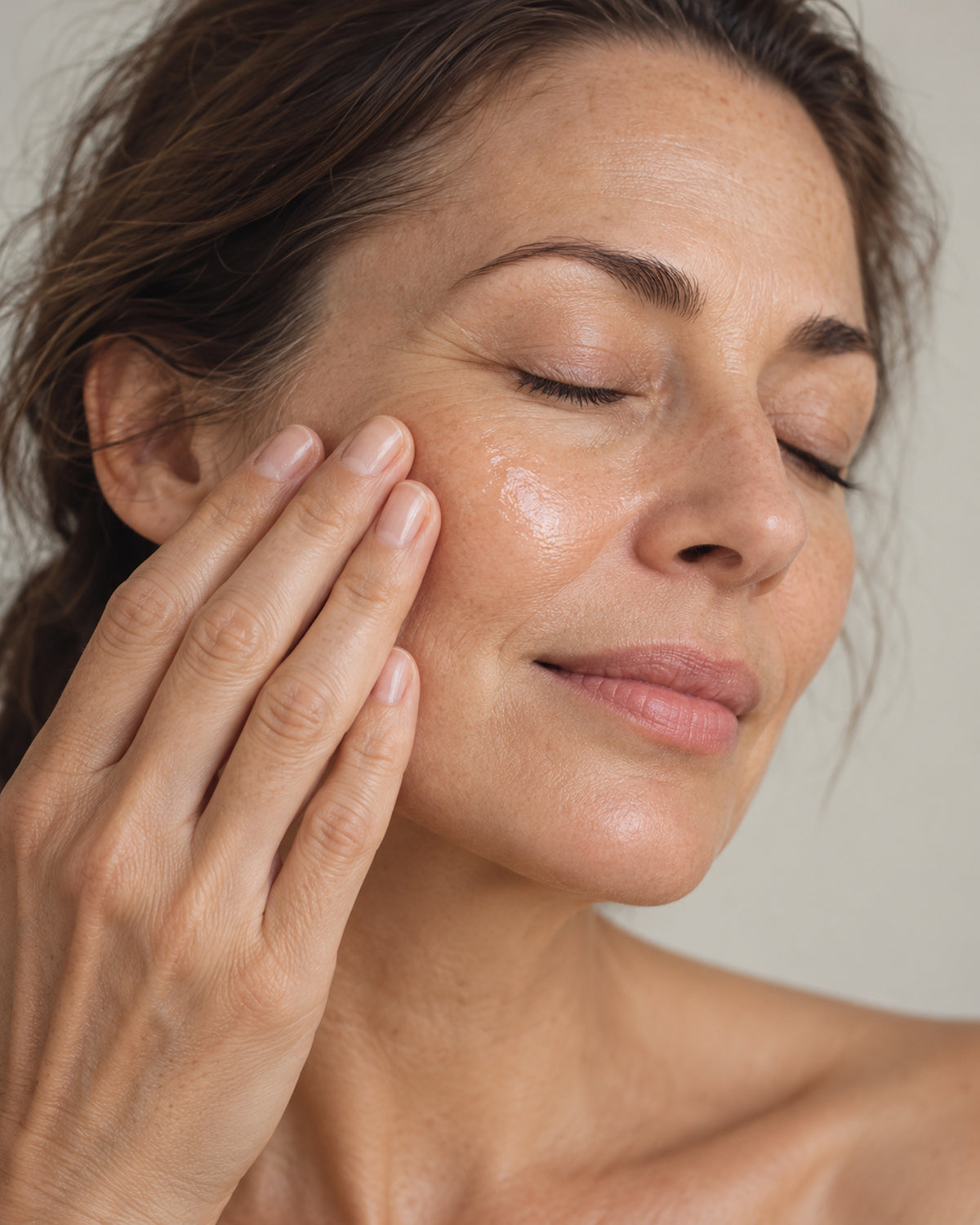 Fingerspitzen klopfen das Serum sanft auf eine Wange, die Augen sind geschlossen.