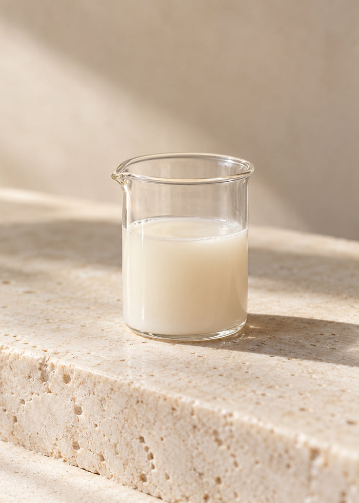 Ein kleines Laborglas mit milchig-heller Flüssigkeit auf hellem Stein.